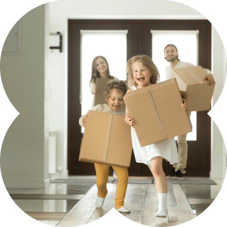 Um casal e seus dois filhos sorridentes carregando caixas de mudança na nova casa da família.