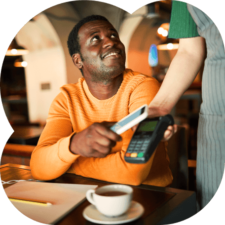 Homem sorridente pagando sua conta no café com o cartão de crédito empresarial Inter por aproximação através de um smartphone